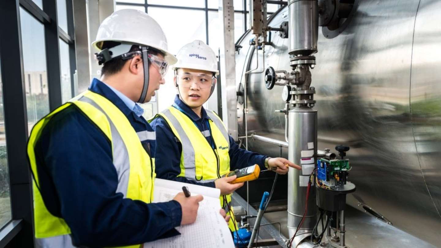 Two engineers stand together wearing hard hats looking at blueprints