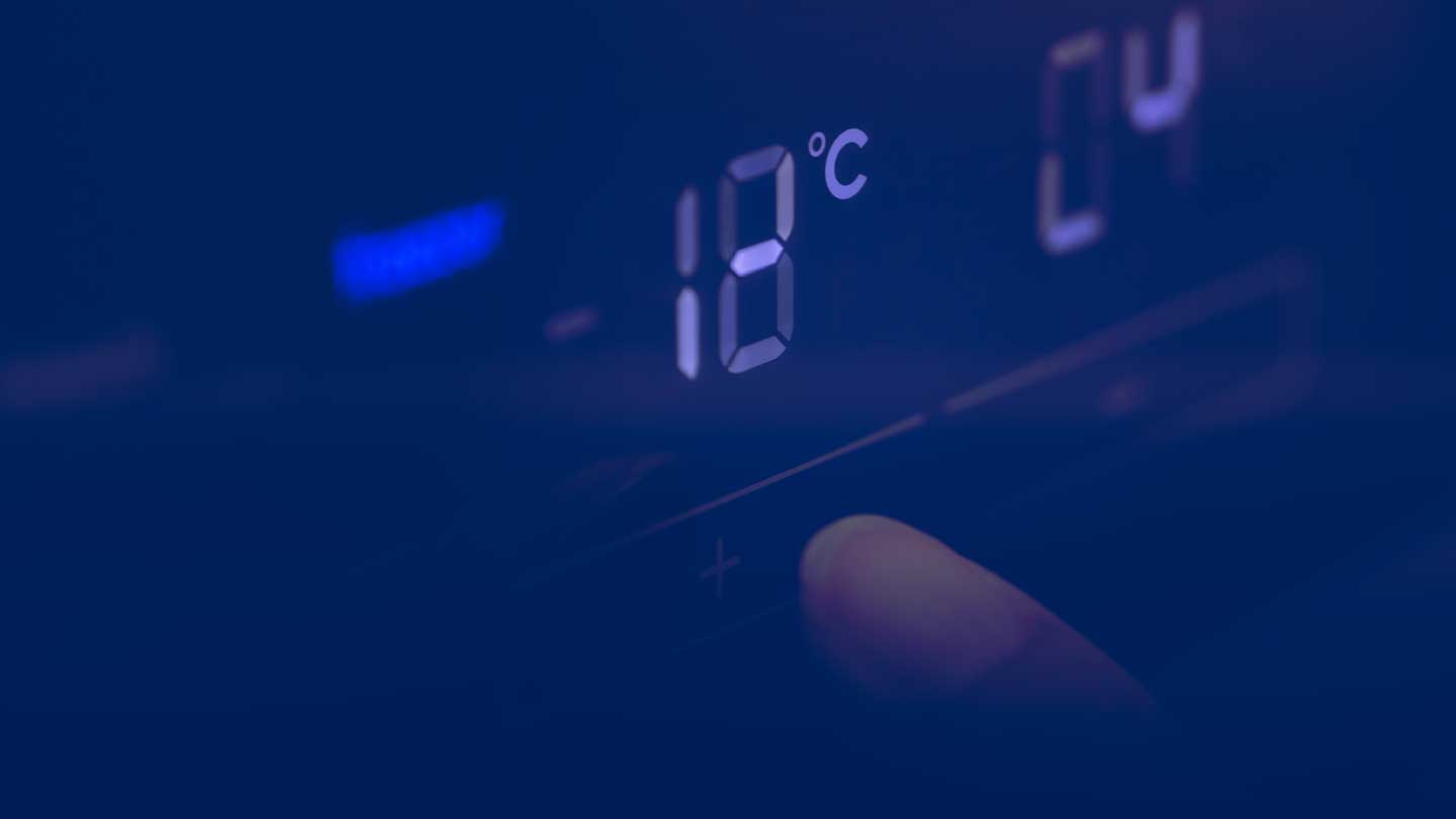 A finger goes to press a button on a thermostat. The temperature is 18 degrees celcius